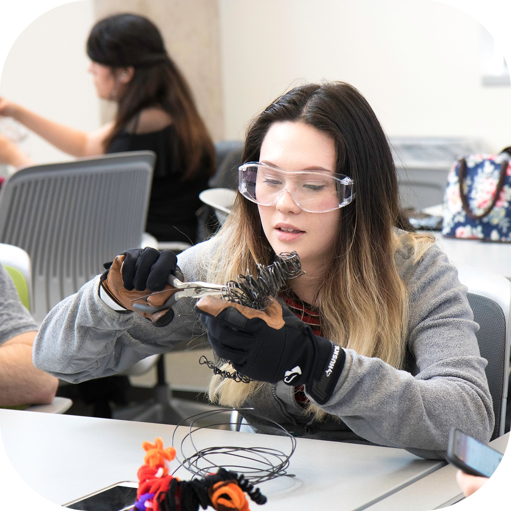 Image of a high school student wearing safety glasses. She is using pliers on a bundle of electrical wires.