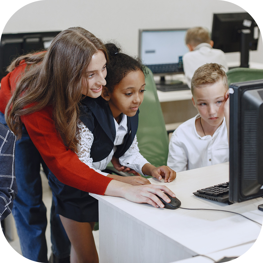 A teacher helps a pair of students use a computer for an assignment.